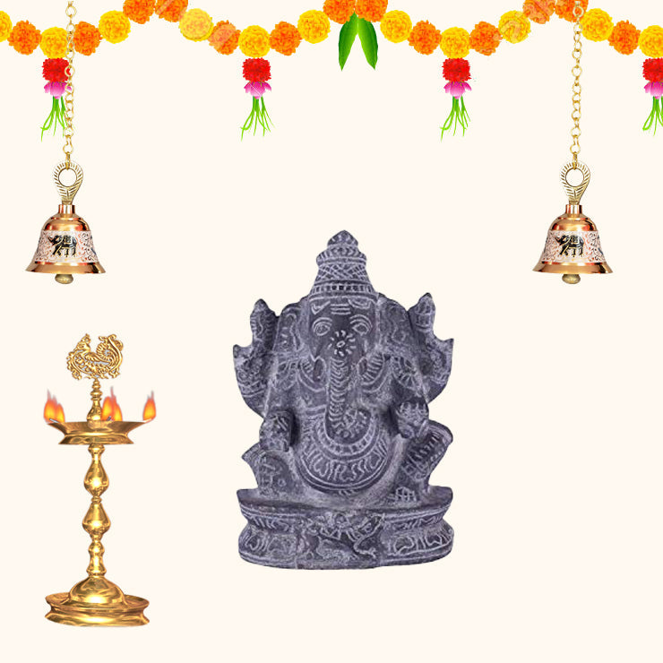 Black stone Ganesha idol with traditional pooja setup, festive home decoration with diya, bells and marigold flowers.
