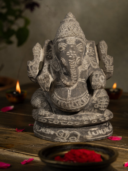 Black Stone Vinayagar Idol in Traditional Pooja Setup with Diyas, Rose Petals, and Tulsi Plant for Home Decor or Vastu Placement.
